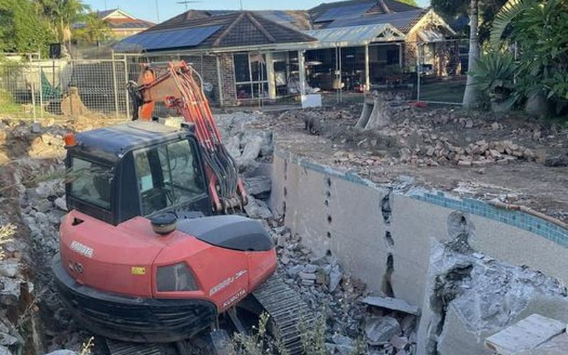 Pool demolition in progress Townsville — excavator breaking up concrete pool shell